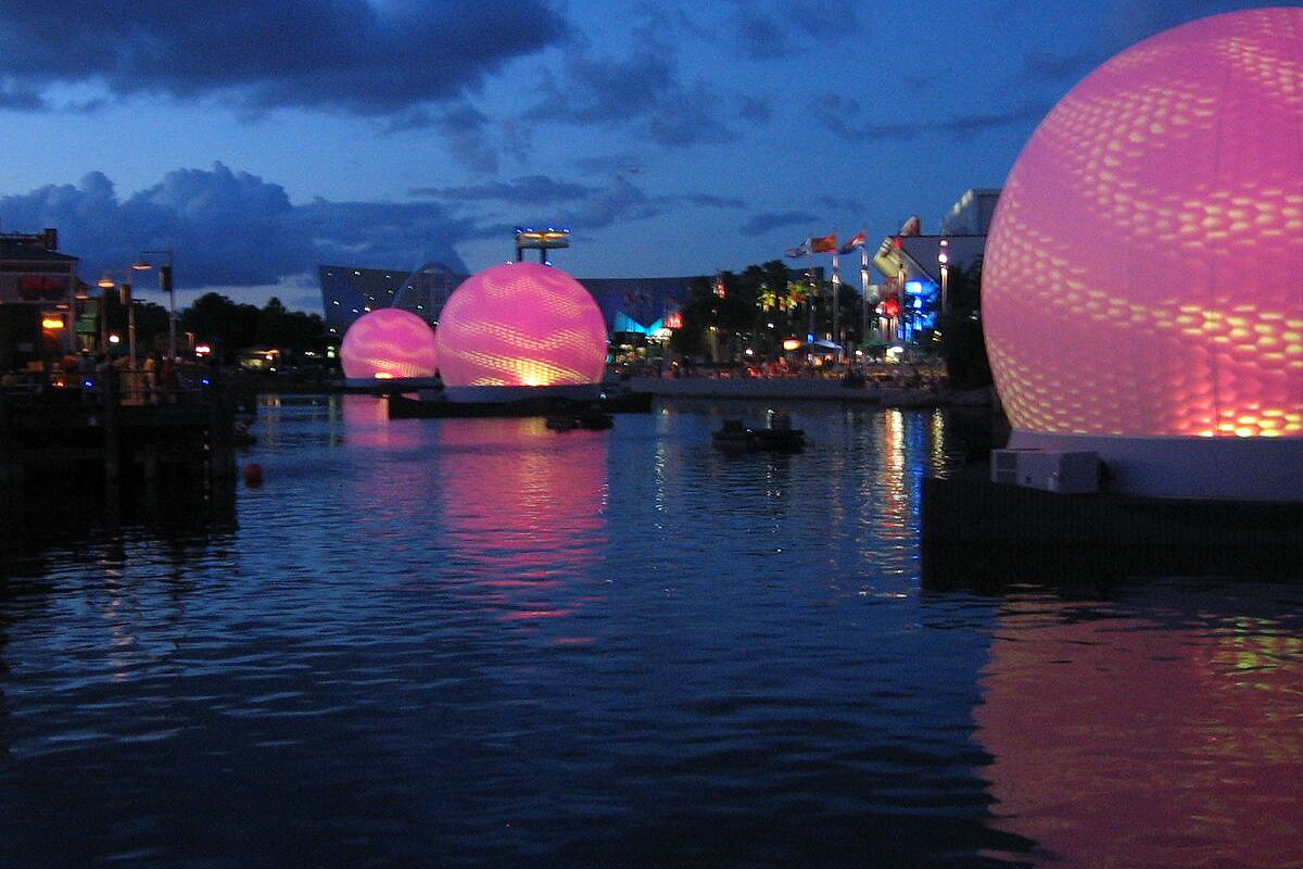 Four Absolute Hollywood Cinesphere projection spheres floating on the Universal Studios Florida lagoon at dusk with pink projection illumination