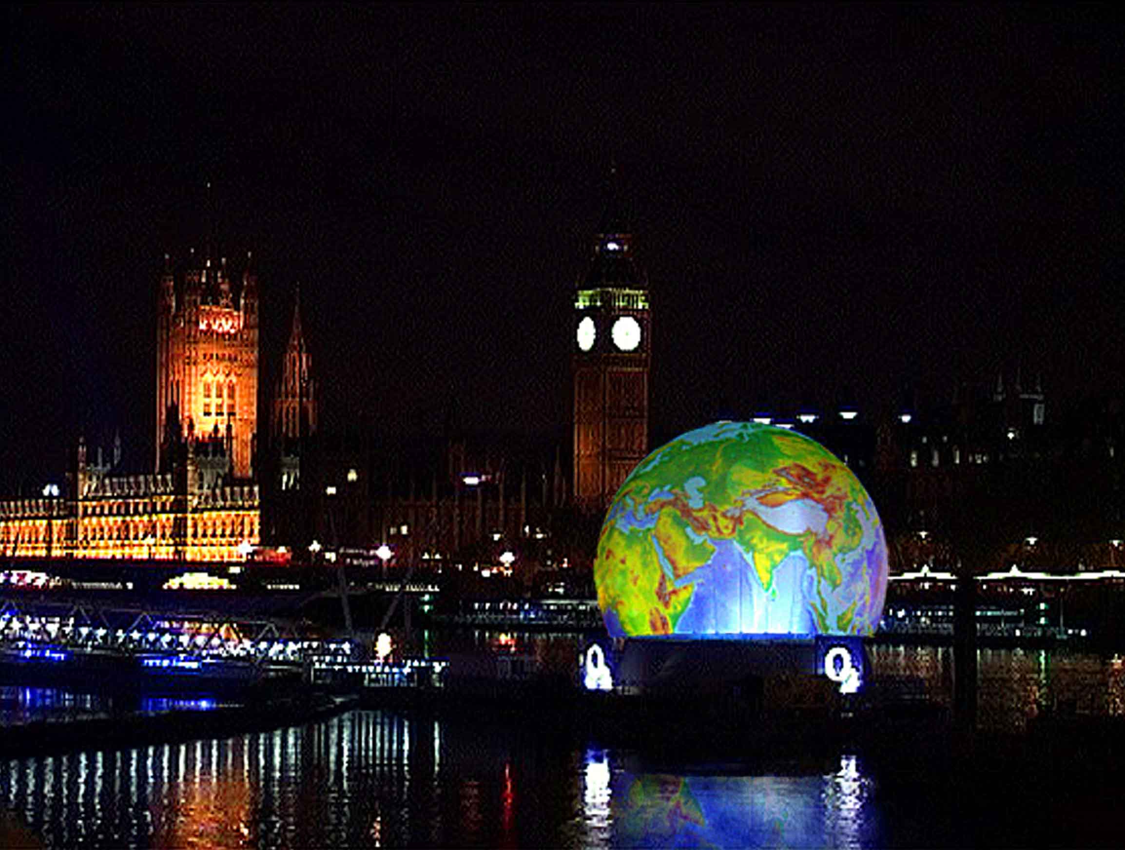 Absolute Hollywood StratoSphere exterior projection sphere glowing blue on the River Thames at night with Big Ben and Houses of Parliament behind it