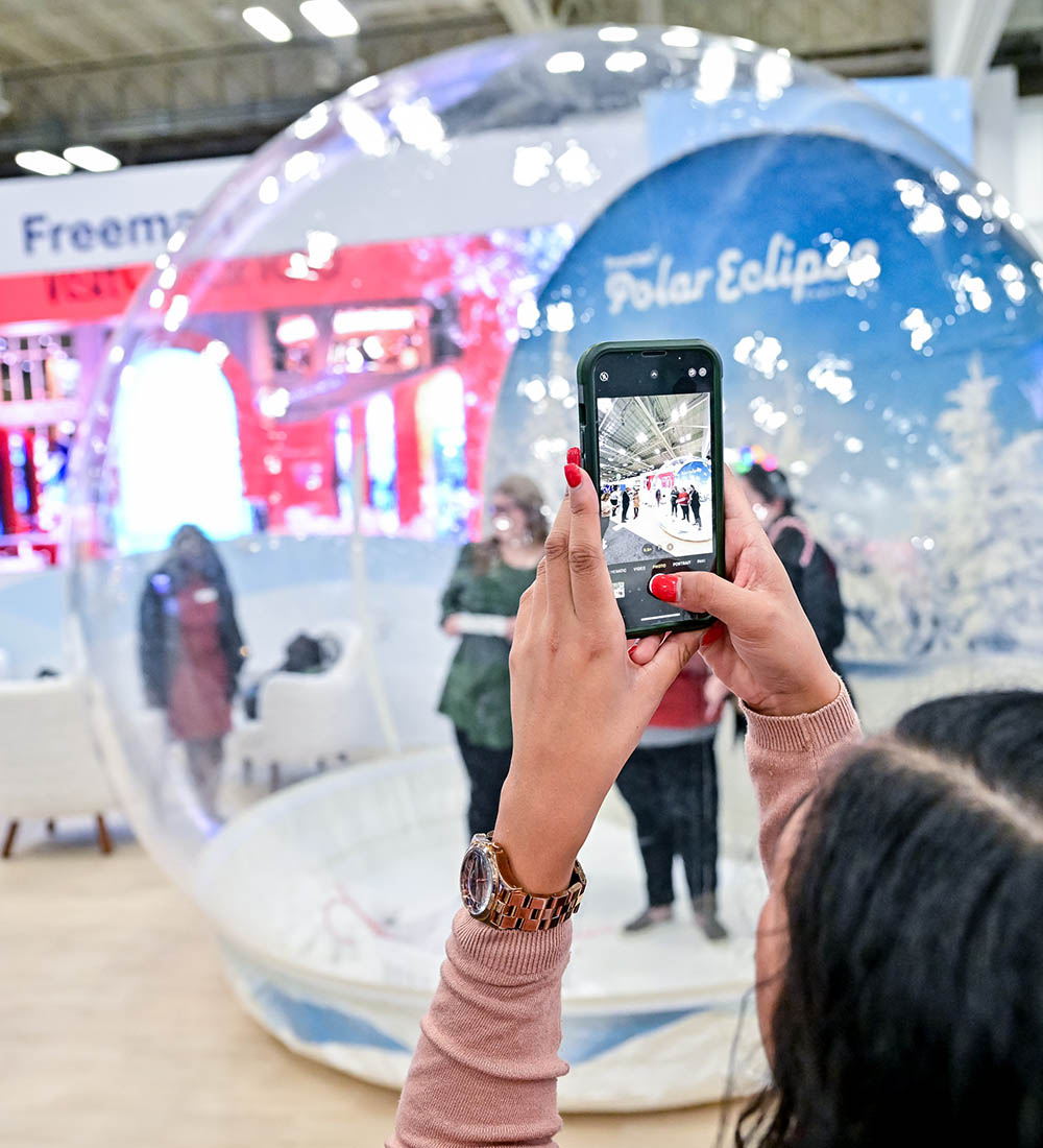 Attendee photographing guest inside Absolute Hollywood inflatable snow globe photo booth at Freeman convention — trade show snow globe rental activation