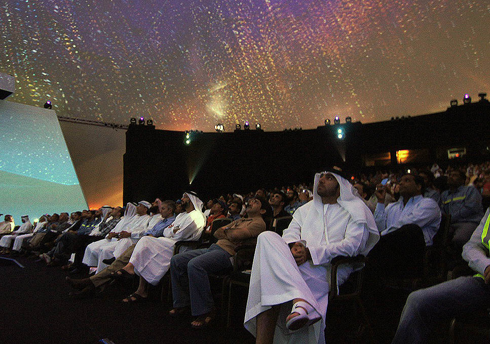 Audience inside Absolute Hollywood Galactic projection dome looking up at 360 degree fulldome projection covering full hemispheric surface, EMAL inauguration Abu Dhabi 2011, attendees in traditional Gulf dress