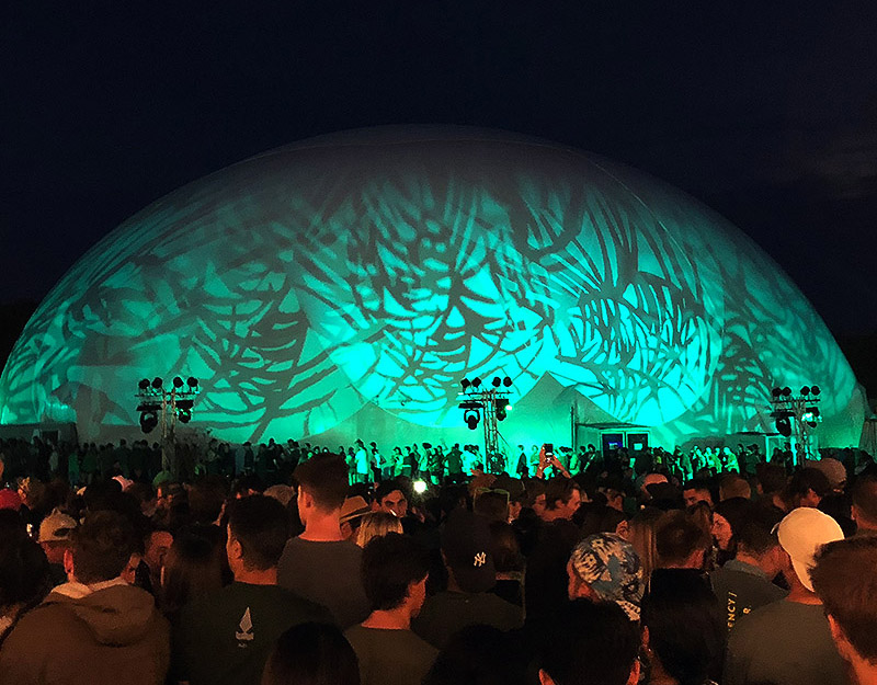 Night festival crowd gathered around the glowing Dome 160 in an open park — Childish Gambino's Pharos, New Zealand