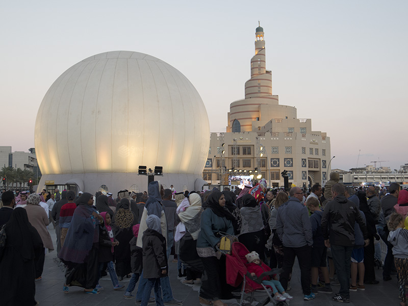 Projection dome exterior — Absolute Hollywood inflatable projection dome deployed on plaza at Souq Waqif, Doha Qatar, with Abdullah Bin Zaid Al Mahmoud Islamic Cultural Center Fanar Masjid spiral minaret visible in background, Children's Festival