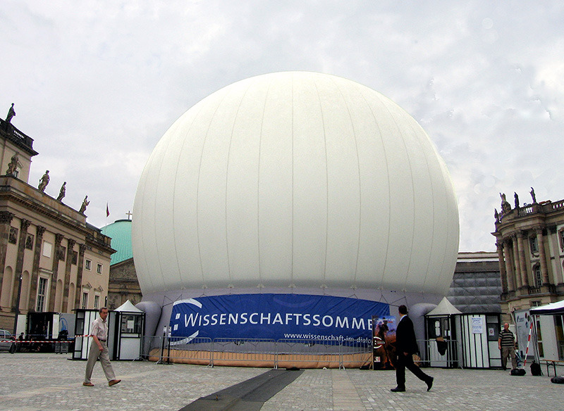Projection dome exterior daytime — large white inflatable projection dome in classical Berlin square flanked by neoclassical architecture, pedestrians showing scale, Einstein Space Opera Wissenschaftssommer Germany