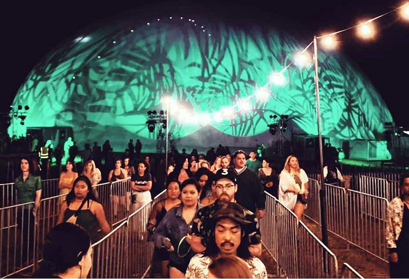 Projection dome exterior night — full 360 degree video projection active on hemispherical dome surface, Childish Gambino PHAROS Festival, Tāpapakanga Regional Park, Orere, Auckland, New Zealand, November 2018, festival crowd in foreground