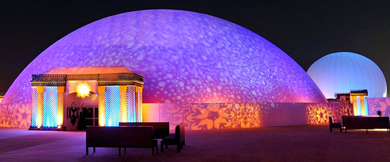 Projection dome exterior night — full 360 video projection firing on Celestial dome surface in purple and blue patterns, Doha Qatar royal wedding with StratoSphere alongside