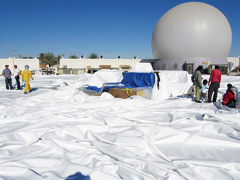 Projection dome setup crew positioning dome fabric on ground before inflation — Absolute Hollywood deployment Doha Qatar with StratoSphere fully inflated in background