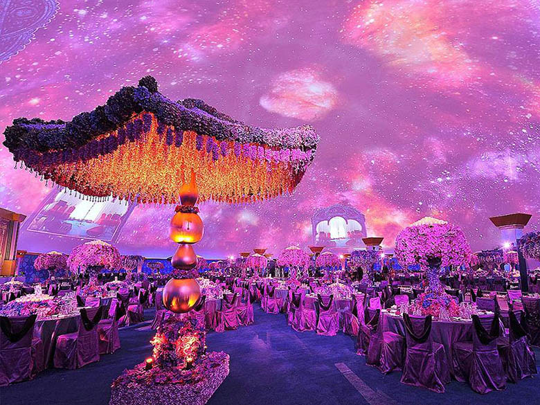 Projection dome interior banquet — galaxy fulldome projection overhead, ornate flower chandelier suspended from dome ceiling, round banquet tables set for royal wedding gala, Doha Qatar