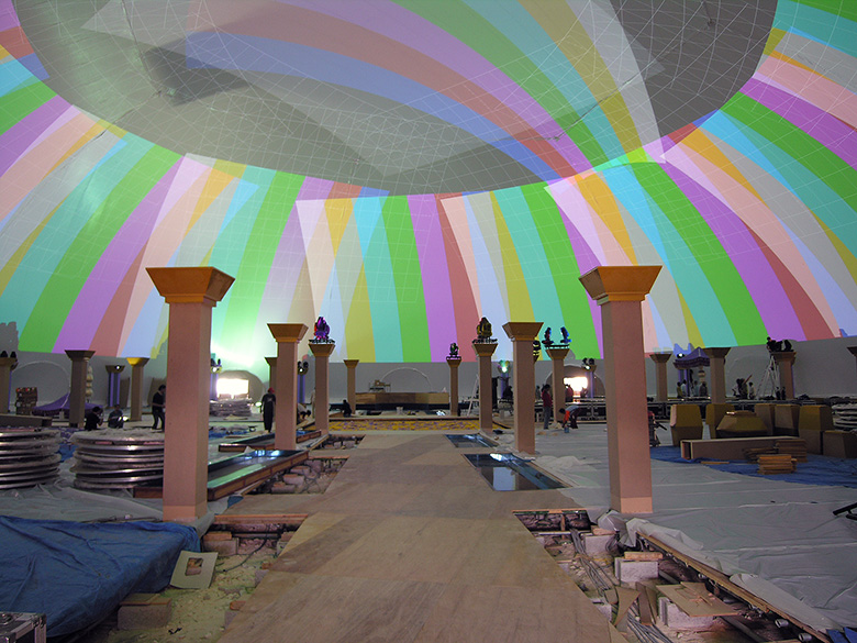 Projection dome interior during setup — full dome projection calibration test pattern covering hemispherical surface with columns and event furniture being positioned, Qatar