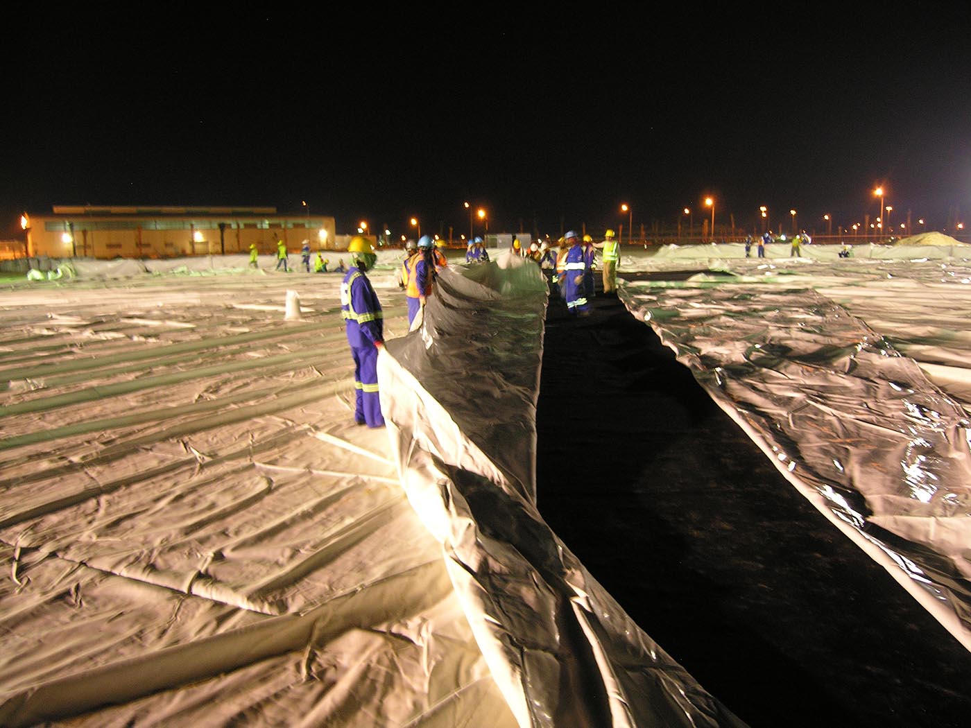 Installation crew spreading air-shippable dome fabric across the night site under work lights ahead of inflation
