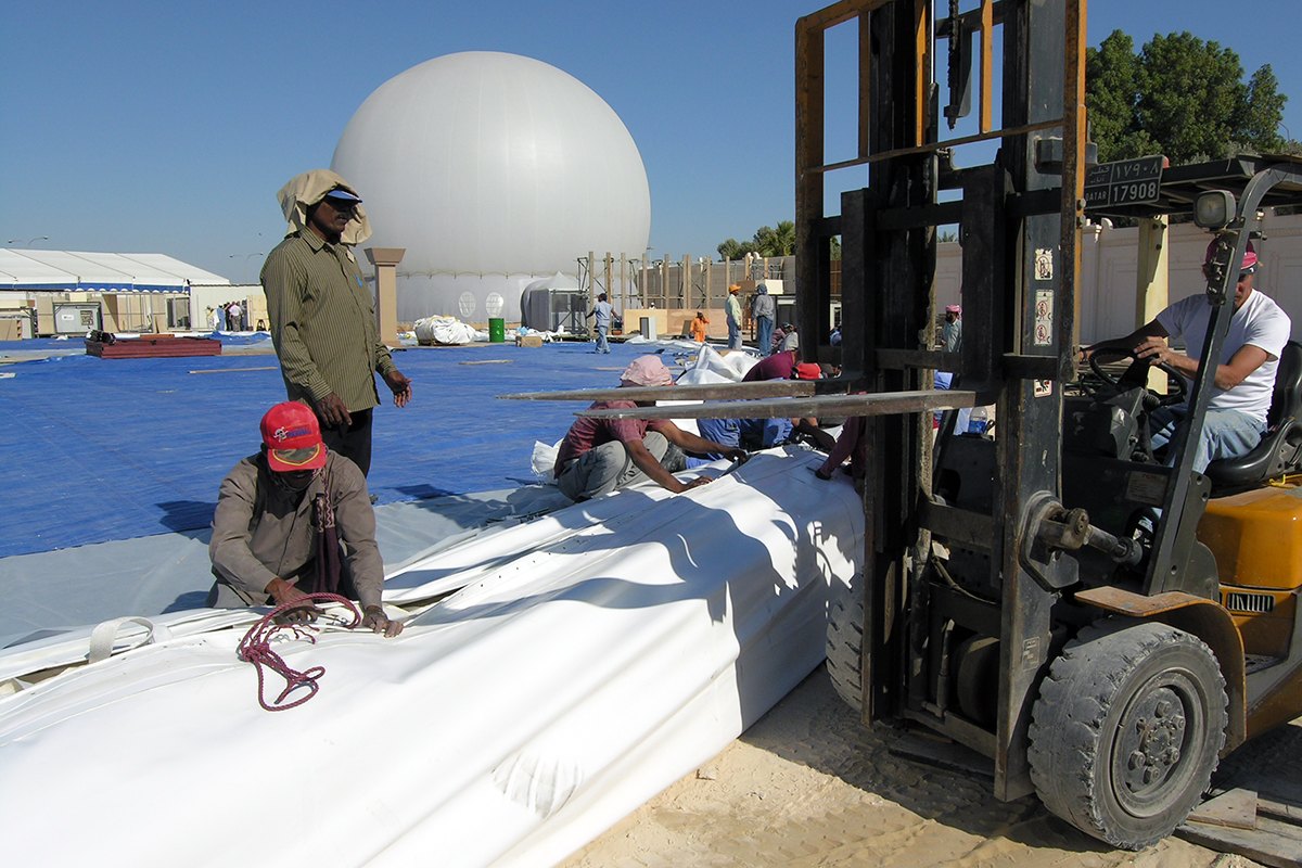Crane-free geodesic dome alternative: ground crew unrolling a 200 ft Celestial dome skin by forklift at the Royal Wedding, Doha, Qatar, with a 60 ft StratoSphere already standing