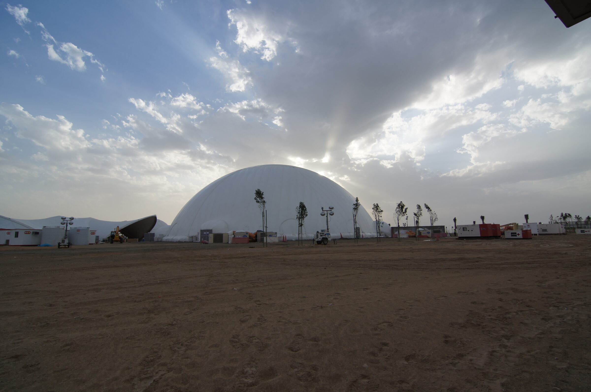 Large white Celestial projection dome rental standing on open desert in the UAE with sunbeams breaking through clouds behind it.