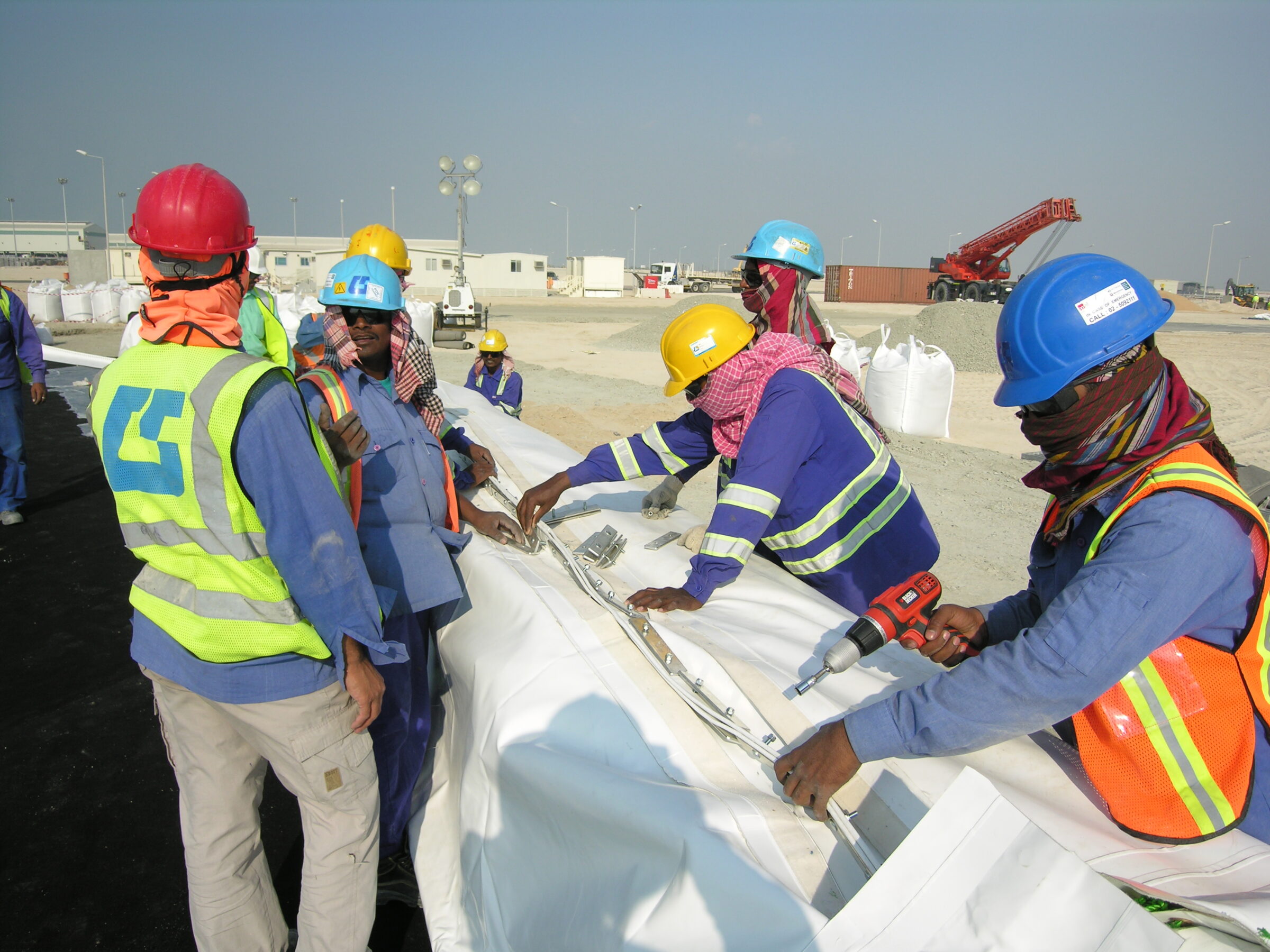 Construction crew in hard hats fastening fabric panels of a Celestial projection dome rental during assembly in the UAE desert.