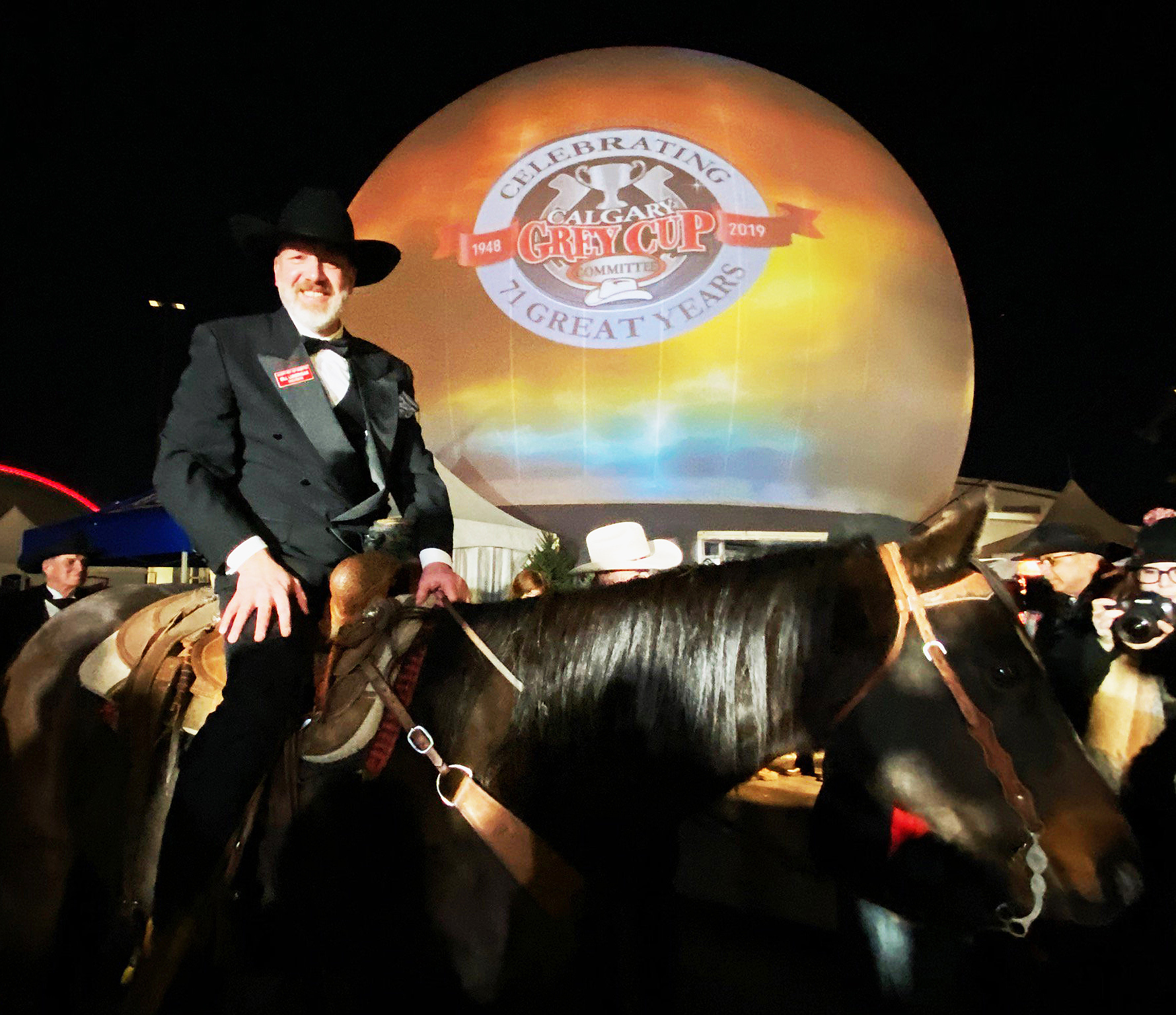 Rider in formal western wear on horseback at night in front of a spherical projection dome rental displaying the Calgary Grey Cup Committee 71st anniversary projection.