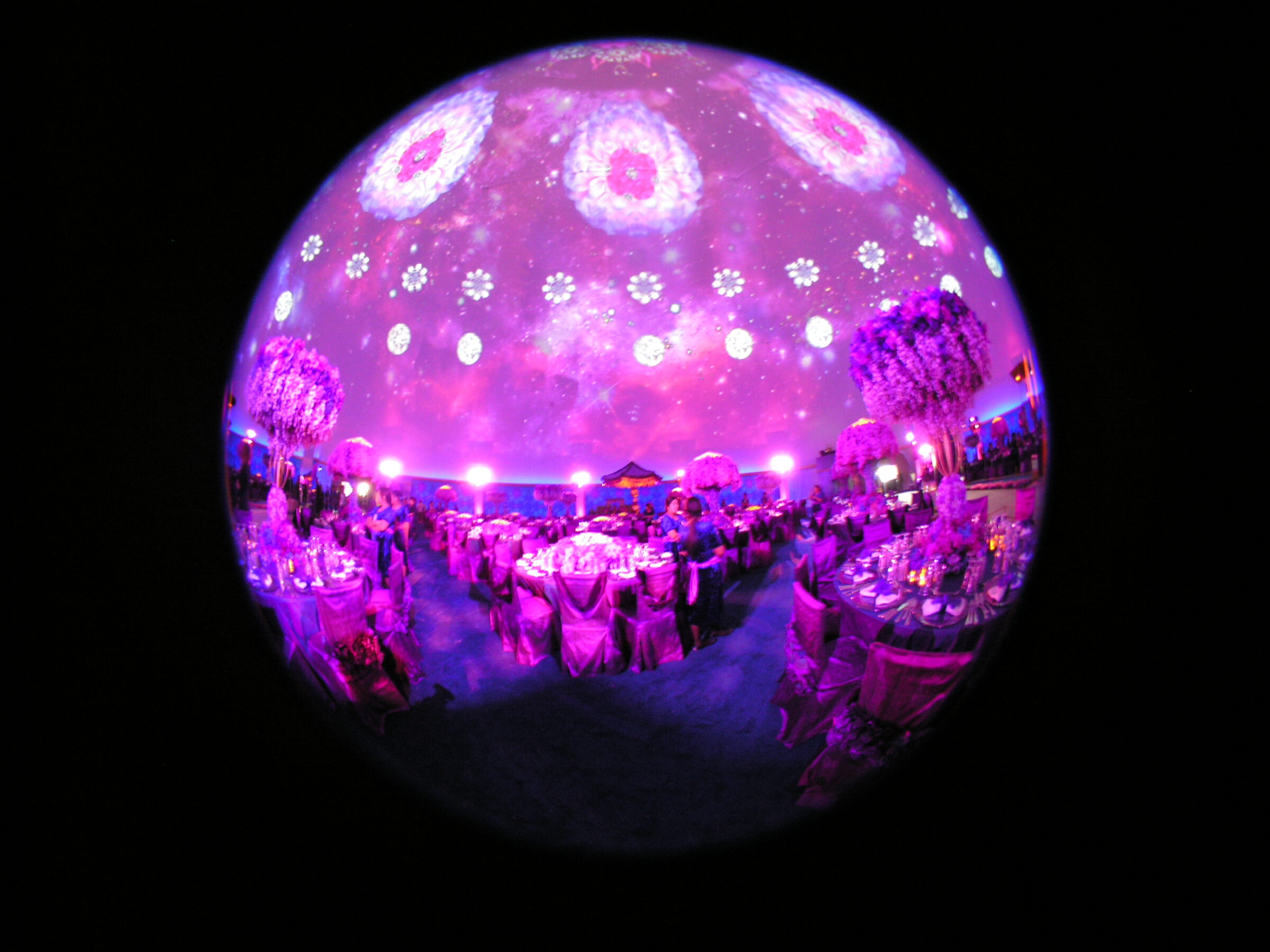 Fisheye view inside a projection dome rental showing pink mandala projection wrapping the full hemisphere over wedding guests in Doha.