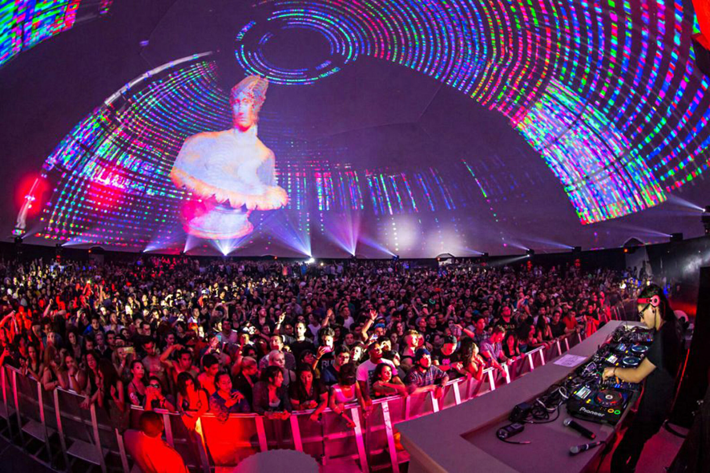 Concert crowd and DJ inside the Celestial projection dome at the LA Coliseum under kaleidoscopic 360-degree projection.