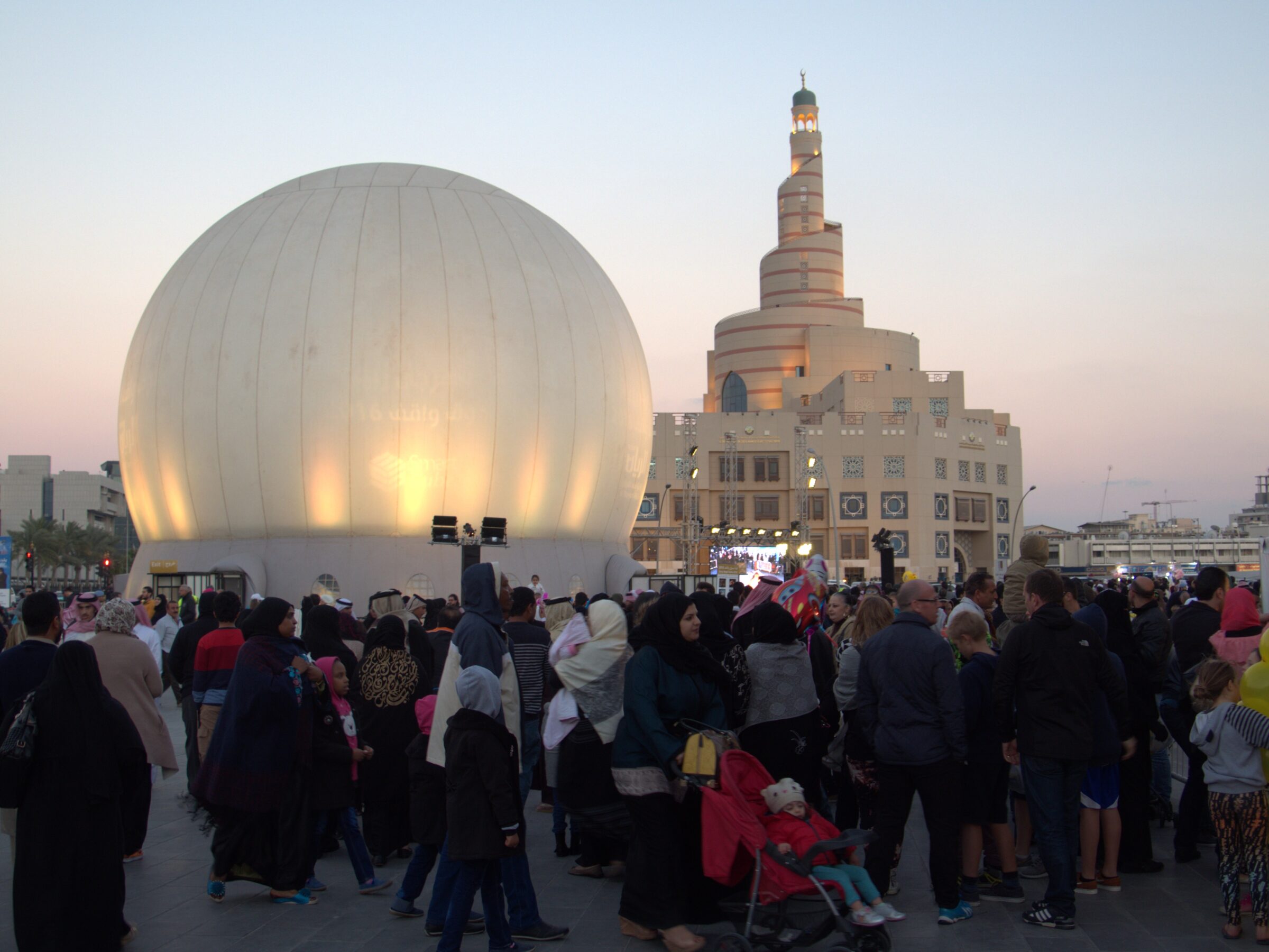 Spherical projection dome rental at dusk during the Doha Spring Festival in Souq Waqif, with the spiral minaret and festival crowds in the fading light.