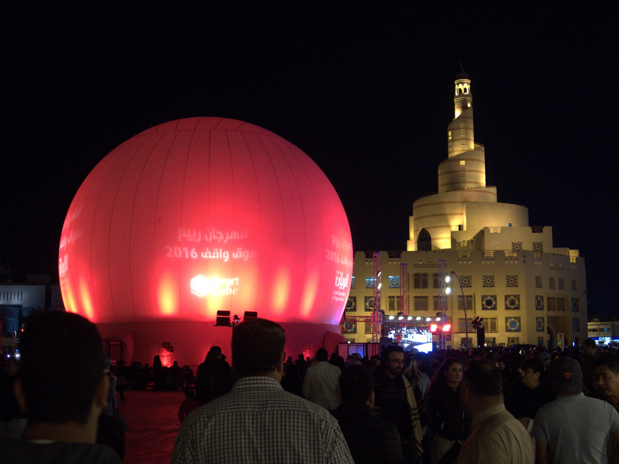 Glowing red spherical projection dome rental at the Doha Spring Festival in Souq Waqif at night, with the spiral minaret lit behind and festival crowds around it.