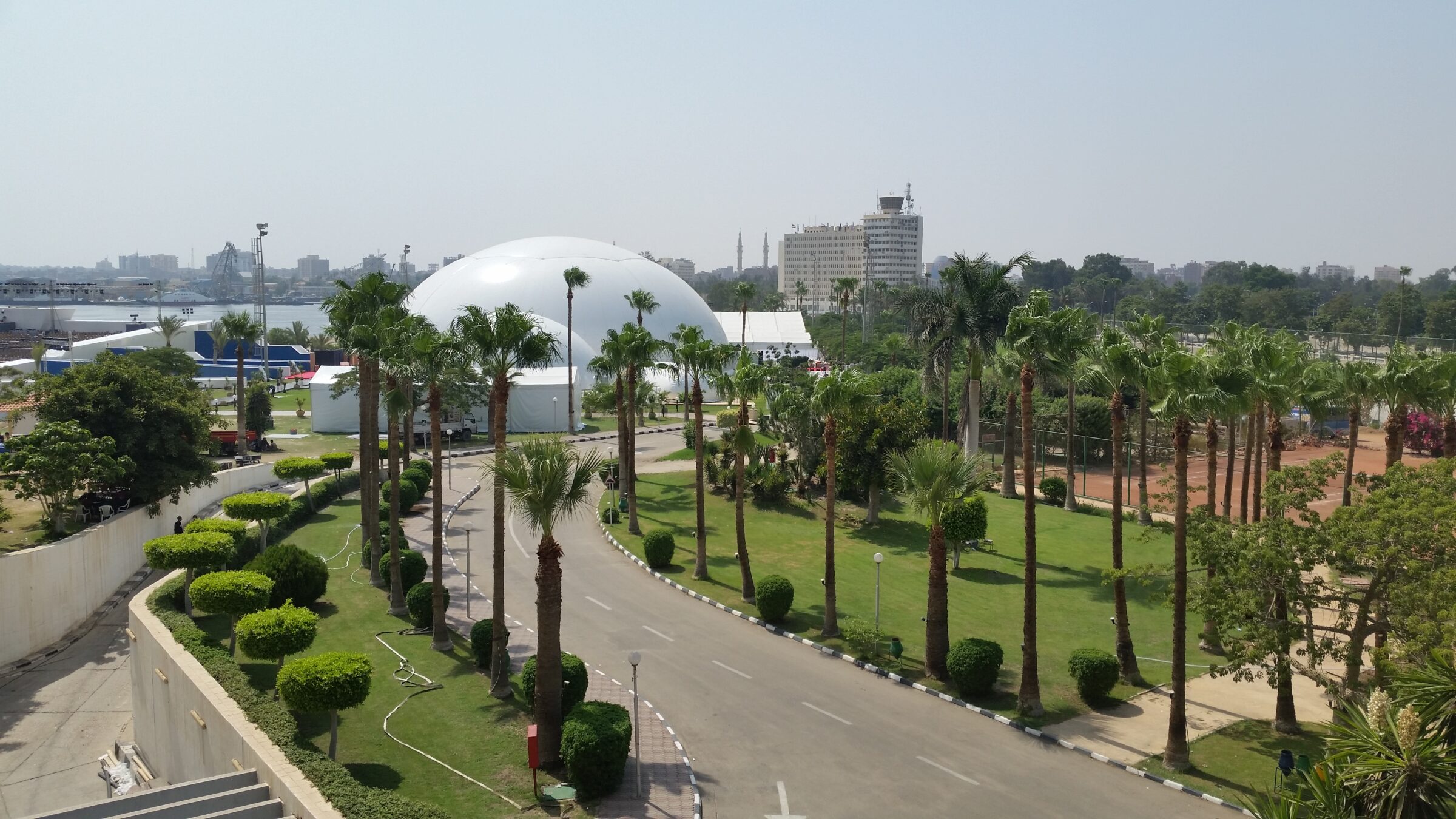 Elevated view of a white projection dome rental among palm gardens at the New Suez Canal Grand Opening ceremony site in Ismailia, Egypt.
