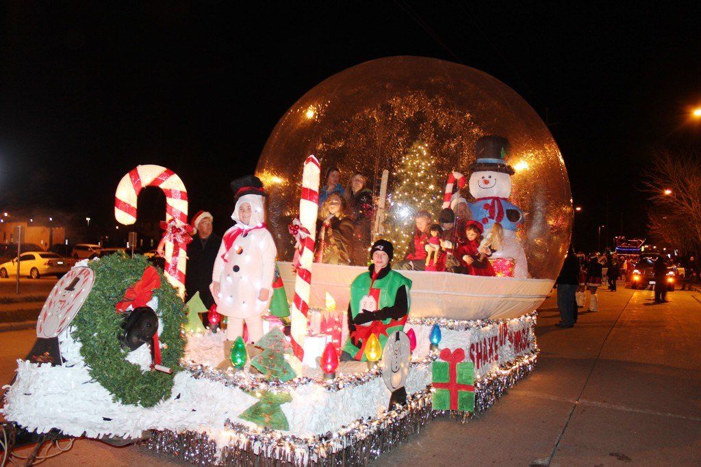 Snow globe rental mounted on a lit parade float at night with candy canes, snowmen and gift boxes around it