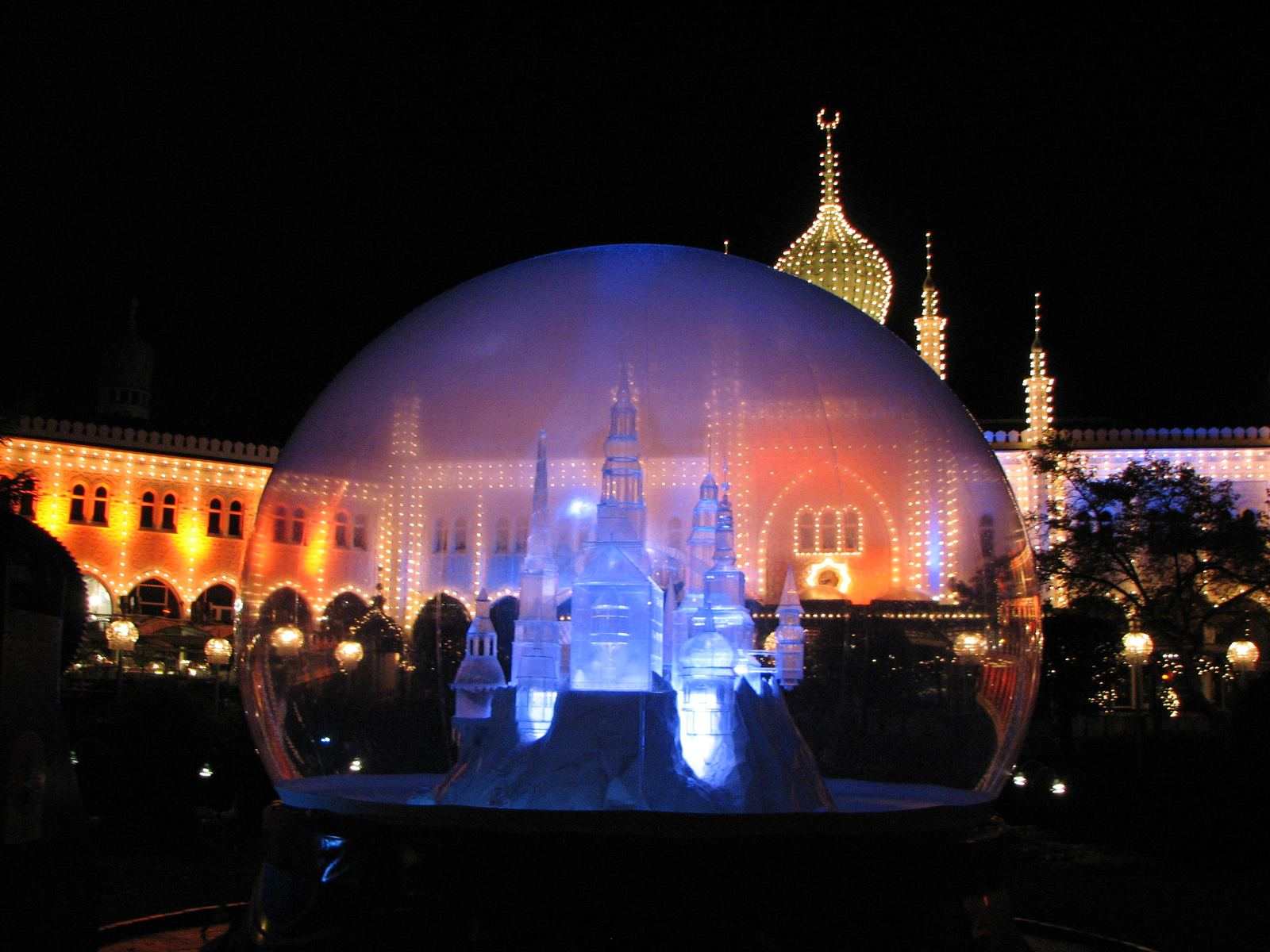 Large illuminated snow globe glowing blue and orange at night in front of a floodlit palace facade in Copenhagen